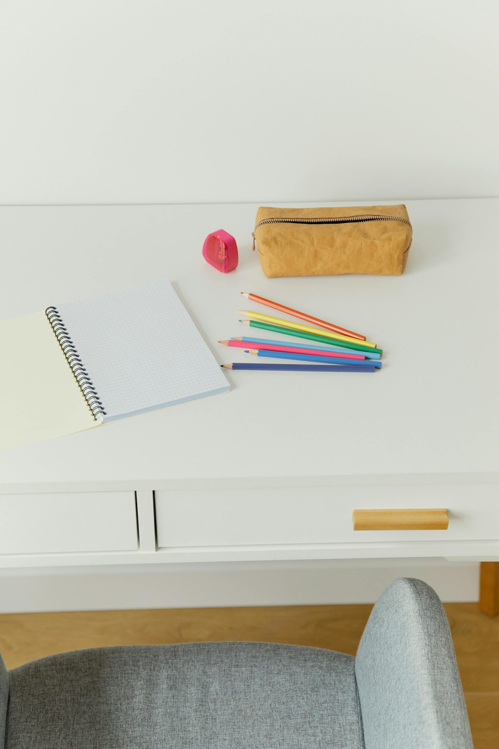 A tidy workspace featuring a notebook, colored pencils, and an eraser on a white desk.